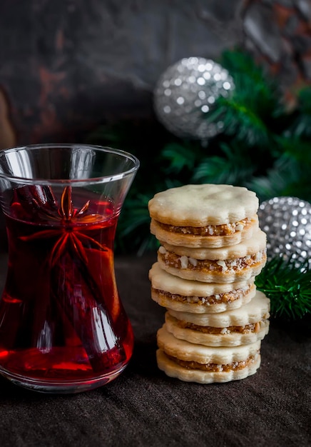 Tea with spices and herbs and shortbread biscuits with caramel cream and walnuts on a dark surface