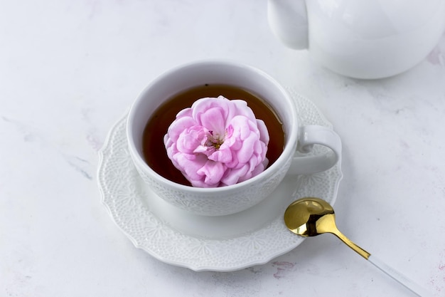 Tea with tea rose in a white cup on a white marble table top\
view