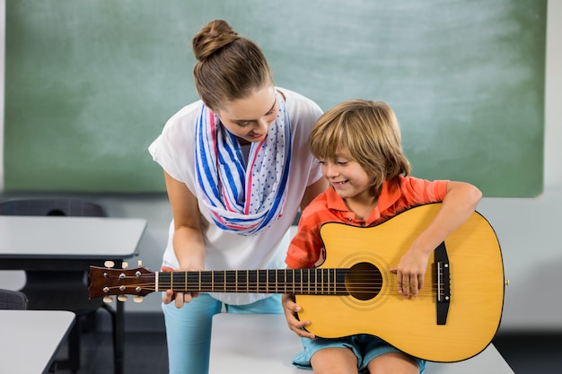 teacher assisting boy to play guitar