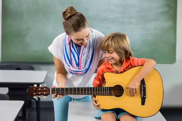 Teacher assisting boy to play guitar