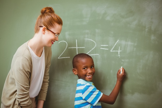 Teacher assisting boy to write on blackboard in classroom