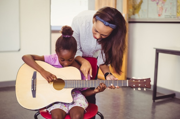 Teacher assisting a girl to play a guitar in classroom