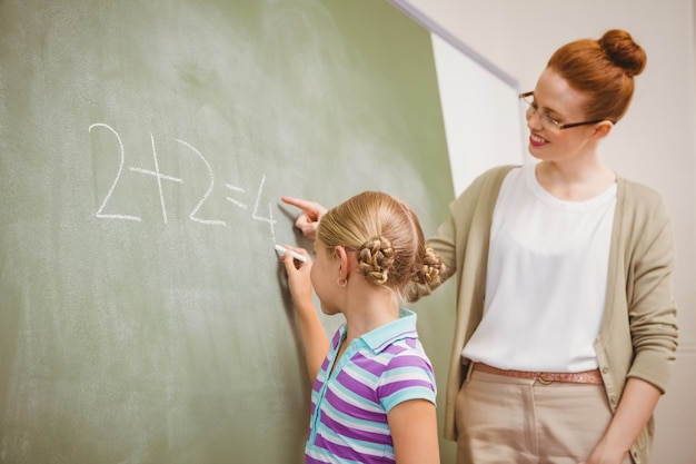 Teacher assisting girl to write on blackboard in classroom