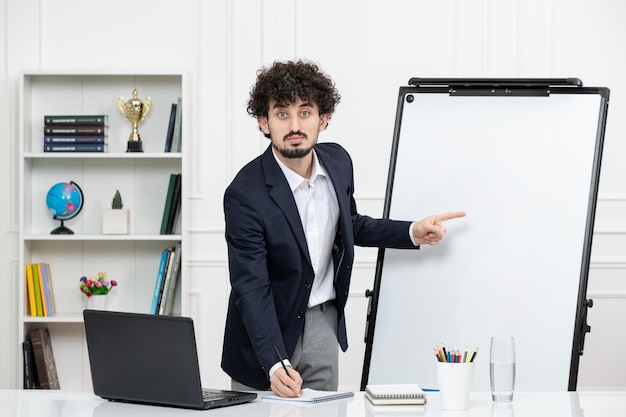 Teacher brunette instructor with computer in suit and whiteboard in classroom looking focused