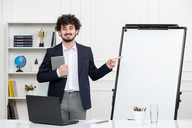 Teacher brunette instructor with computer in suit and whiteboard in classroom pointing at board