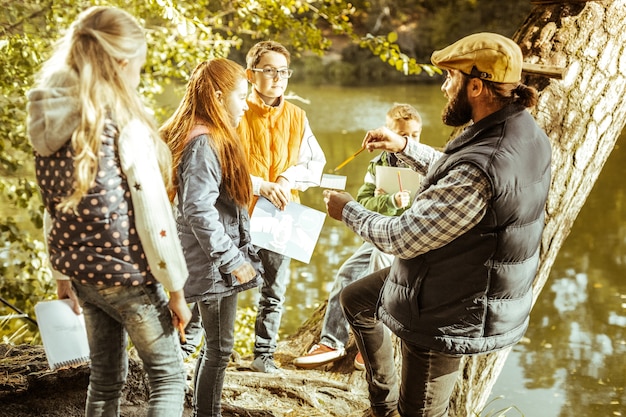 Teacher explaining ecology issues to his pupils in forest on a good day