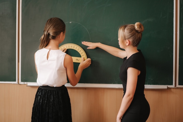 Teacher help girl by the blackboard. Young female teacher study