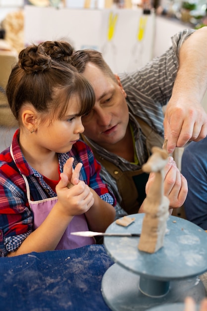 Teacher helping cute pupil sculpting clay animal at art lesson