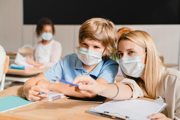 Foto insegnante che aiuta il suo allievo allievo scolastico che spiega materiale nuovo argomento compito modulo test indossando maschera protettiva contro il coronavirus covid-19 l'istruzione scolastica durante la pandemia