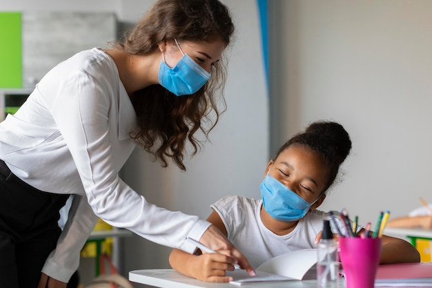 Insegnante che aiuta il suo studente mentre indossa maschere mediche