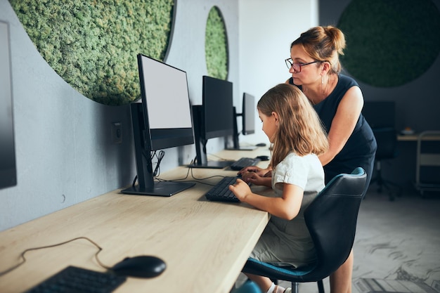 小学校でコンピューターの授業をしている女の子を助ける教師が授業で学習する学校に戻ります