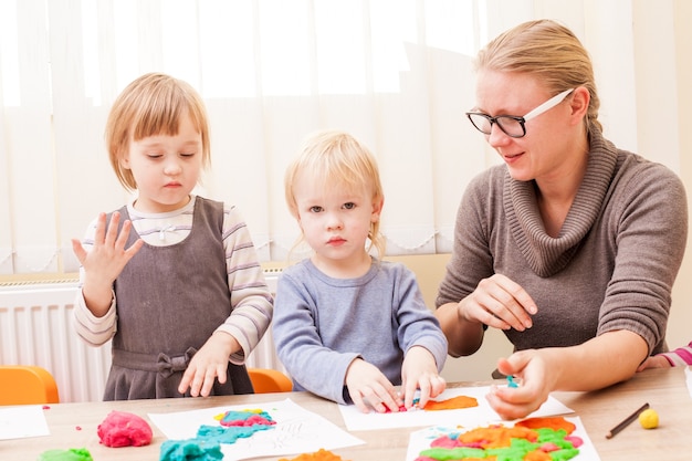 The teacher helps the boy to make a figure plasticine on the table