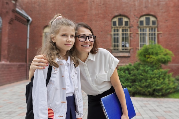 Teacher hugging child near school building. Back to school, start of classes