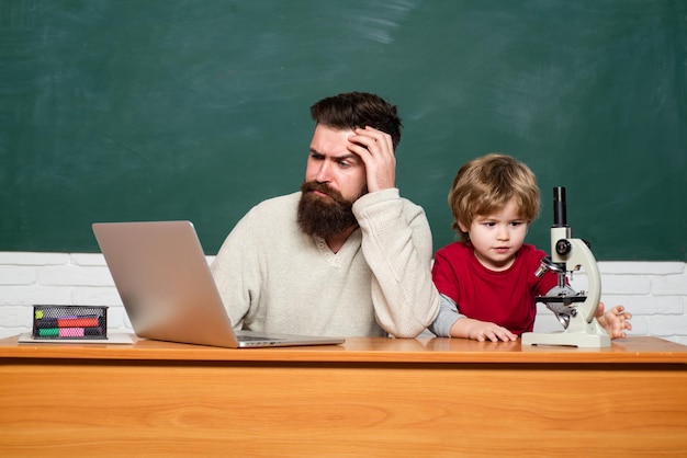 Teacher and kid father teaching her son in classroom at school Teacher helping young boy with lesson Teacher helping pupils studying on desks in classroom Teacher and child