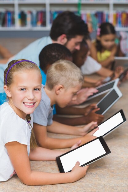 Teacher and kids lying on floor using digital tablet in library