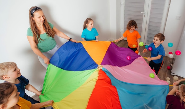 Teacher and kindergarten kids playing with colorful parachute