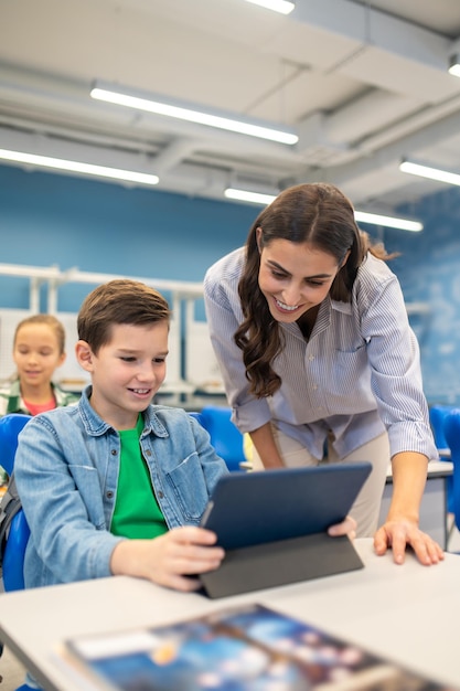 Teacher leaning over tablet of studying boy