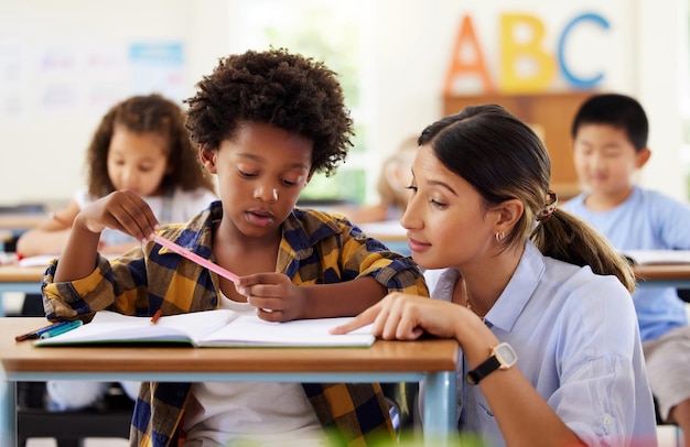 Teacher learning and helping black kid in classroom for knowledge studying or assessment Teaching development and boy or student with woman for education answer in notebook in kindergarten