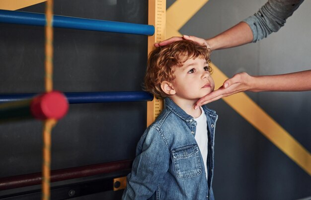 Teacher measuring kids height indoors in kindergarten