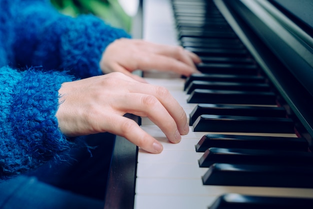 Teacher pianist musician rehearsing classical music. Professional musician lifestyles indoors. Unrecognizable woman playing the piano. Detail of female hands touching a keyboard at home.