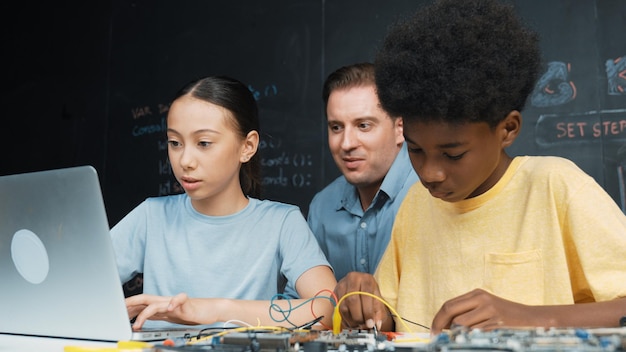 Photo teacher pointing at laptop while teaching about engineering code edification