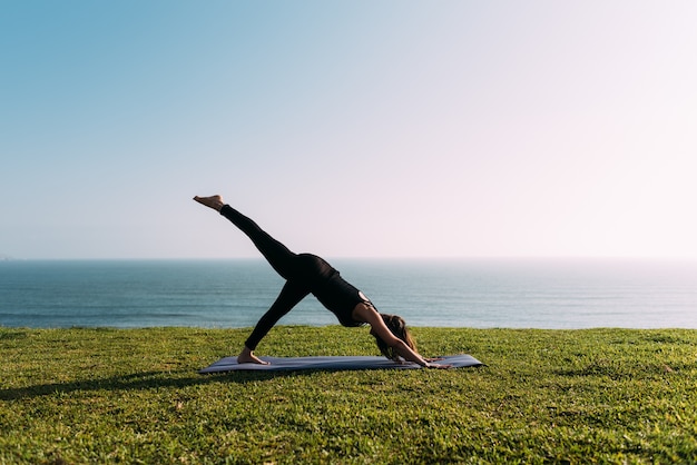 Teacher practices yoga on the lawn in front of the sea. Copy space