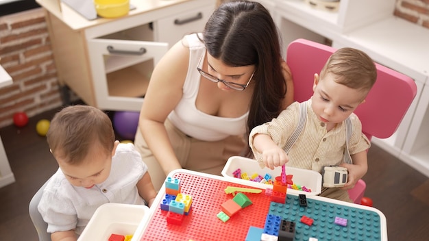 Teacher and preschool students playing with construction blocks and cars sitting on table at kindergarten