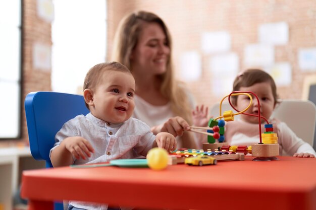 Teacher and preschool students playing with toys sitting on table at kindergarten