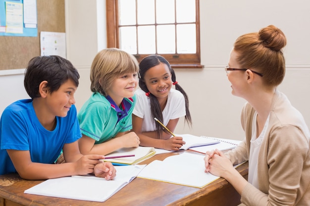 Teacher and pupils working at desk together 