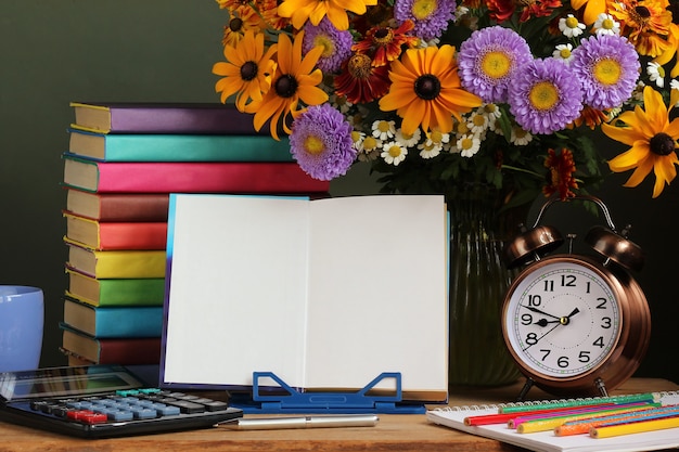 Teacher's day, September 1. Back to school. A bouquet of fall flowers, an alarm clock and an open book on a stand. 