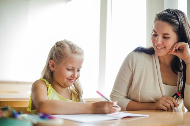 Photo teacher and schoolgirl sitting at table smiling