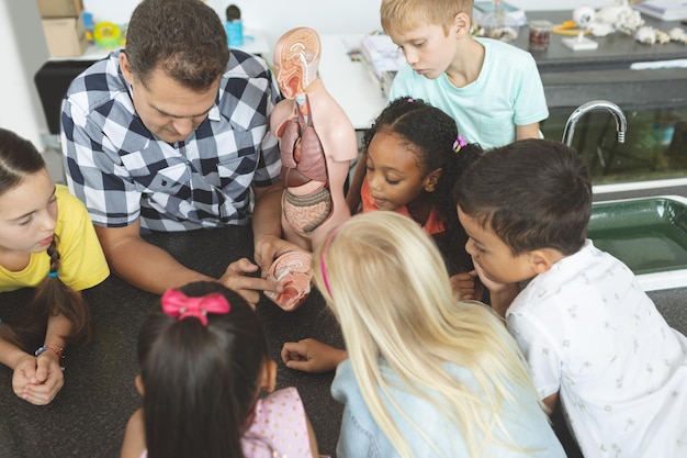 Teacher showing to his school kids a brain part of a dummy skeleton wile they are looking at it