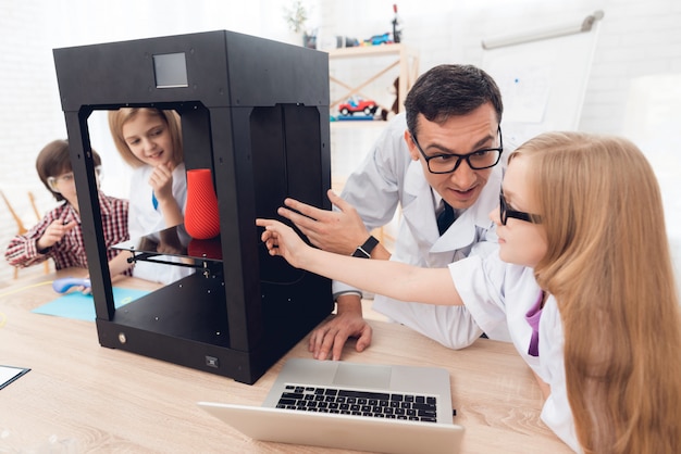 The teacher shows the children how the 3D printer works.