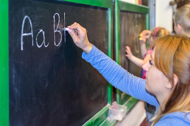 교사는 아이들에게 학교에서 칠판에 알파벳 글자를 쓰는 방법을 보여줍니다