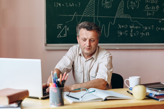 Teacher sitting at the table  in the classroom,working on the laptop