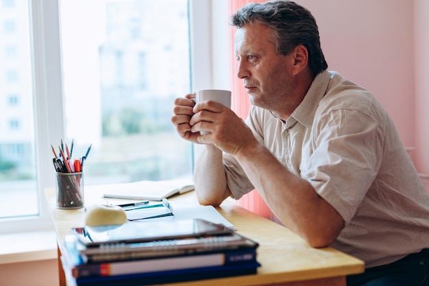 Teacher sitting at the table holding a cup in the classroom and have a rest.