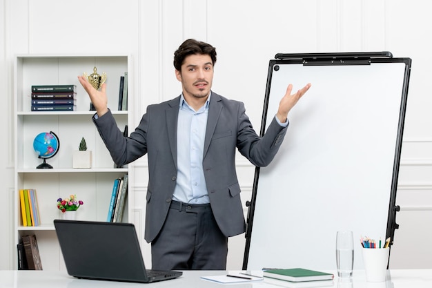 Teacher smart instructor in grey suit in classroom with computer and whiteboard waving hands