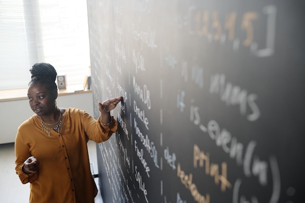 Teacher standing at blackboard at class