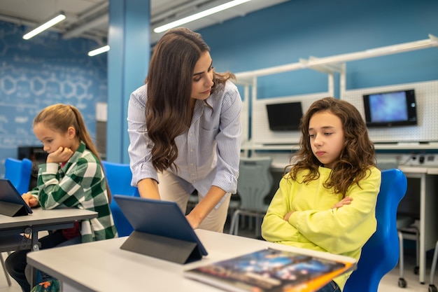 Photo teacher standing near sad girl sitting at desk