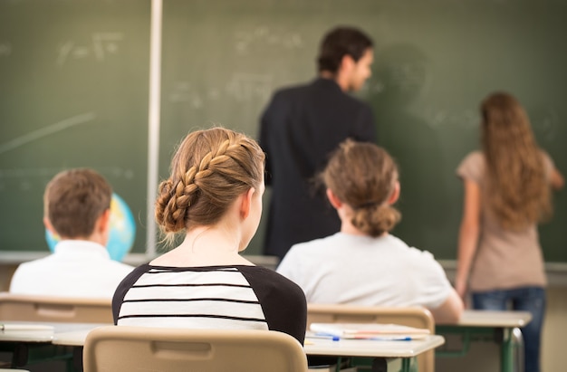 Teacher standing while math lesson  in front of a blackboard and educates students in a school