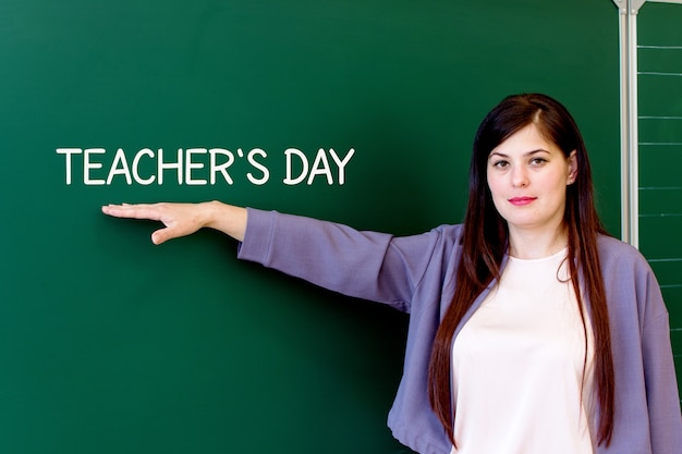 The teacher stands at the blackboard and points to the inscription teachers Day