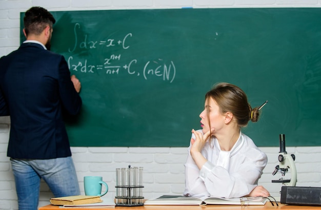 Teacher and student near chalkboard college university\
education high school solving task man writing on chalkboard math\
formulas teaching in university university education knowledge\
transfer