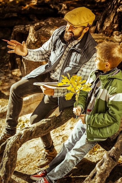 Teacher and student sitting among tree roots in forest having a\
lesson on a fine day