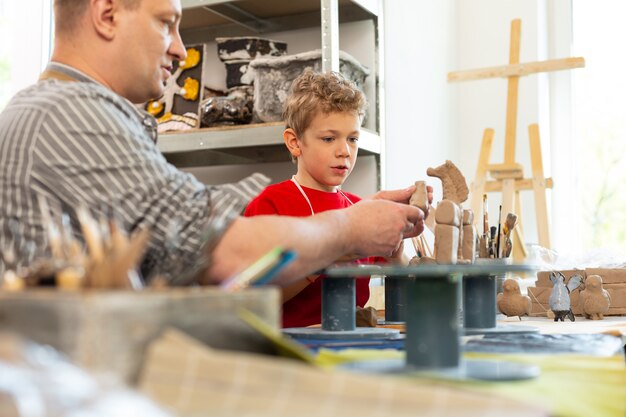 Teacher talking to his talented student sculpting clay figures