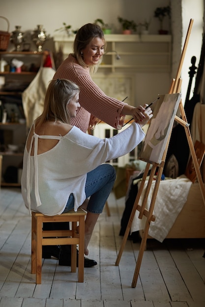 The teacher teaches a young girl to paint on canvas