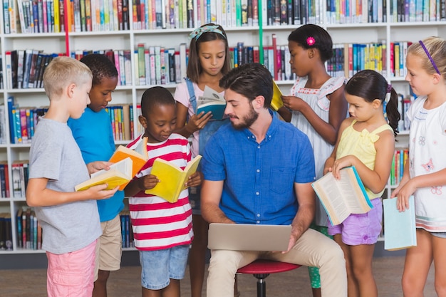 Teacher teaching kids on laptop in library