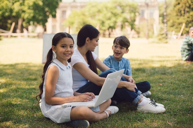 Teacher and two young students use laptop in park