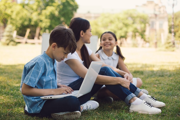 Teacher and two young students use laptop in park