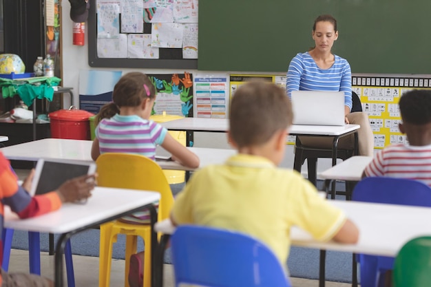 Учитель использует ноутбук в классе, пока школьники учатся