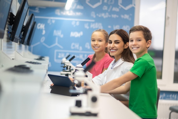 Teacher with children near microscope smiling at camera